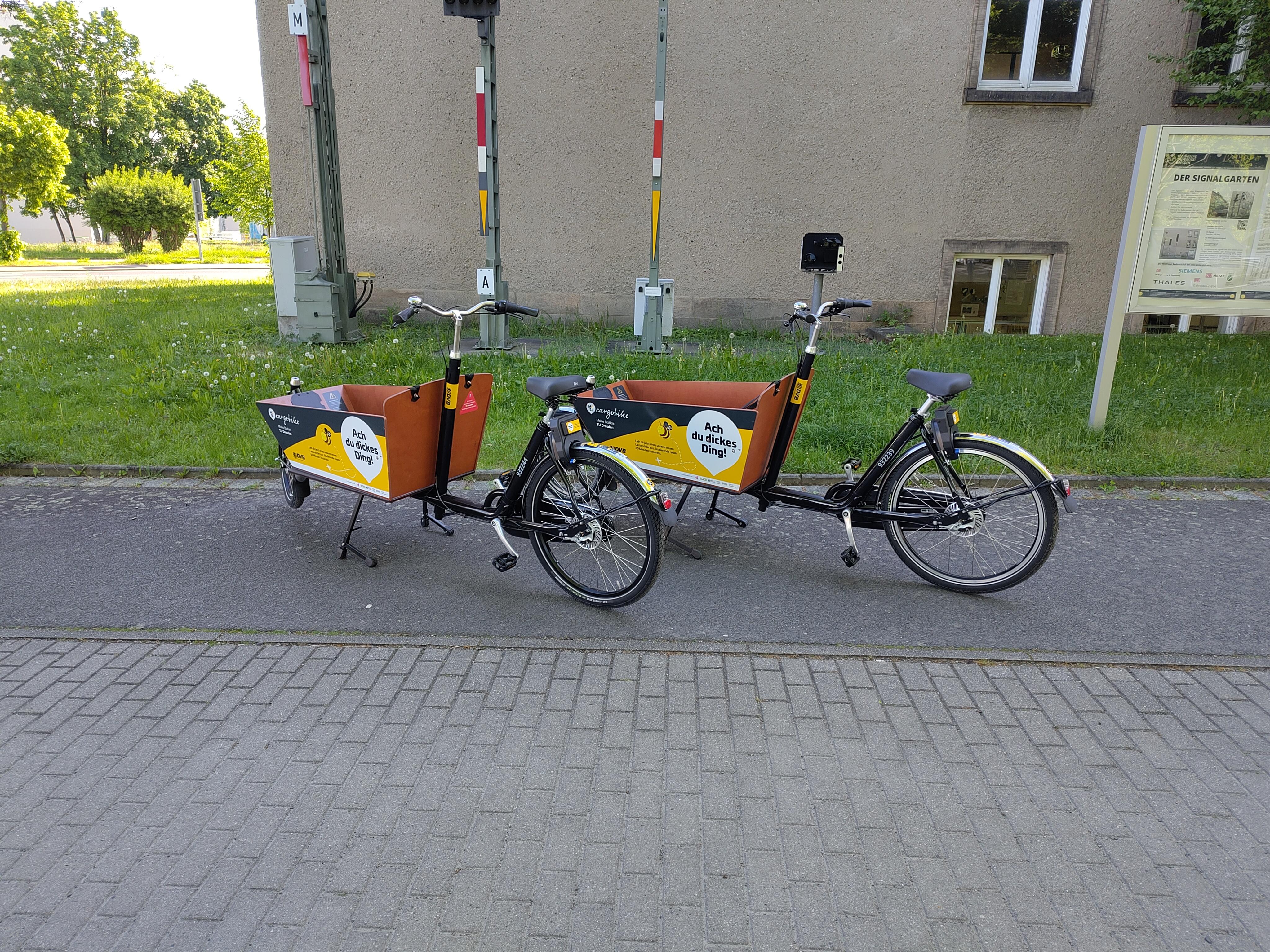 Auf dem Foto sind zwei Lastenräder (MOBIcargobikes zu sehen) vor einer Wiese am Potthoff-Bau zu sehen