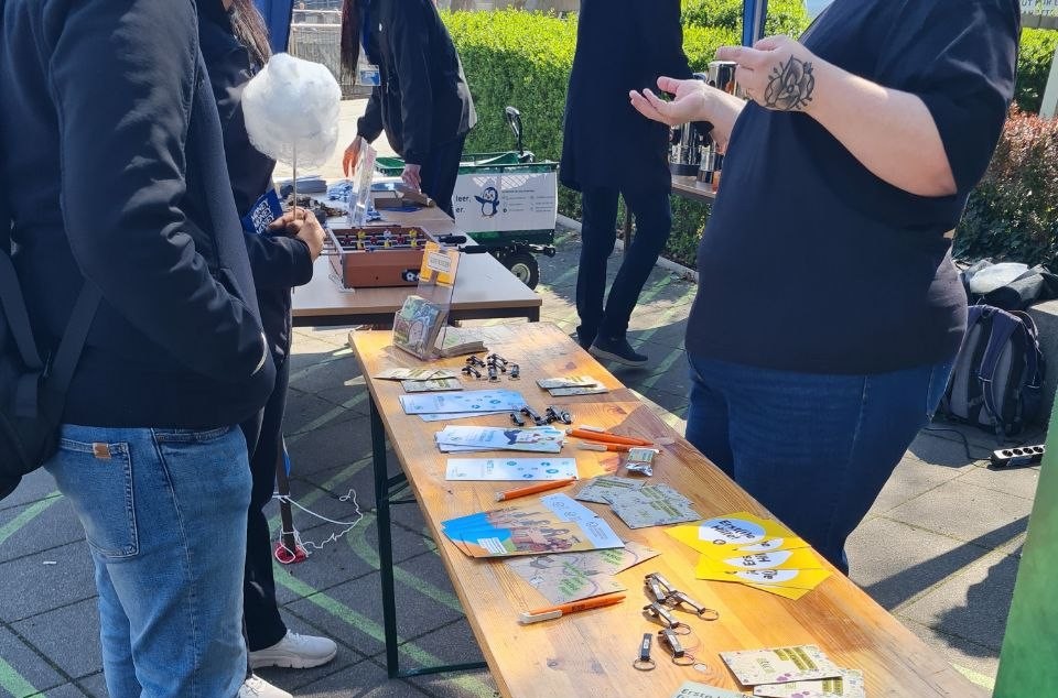 Auf dem Bild sieht man einen Stand vor dem HSZ. Auf dem Tisch liegen viele Infomaterialien und Goodies.
