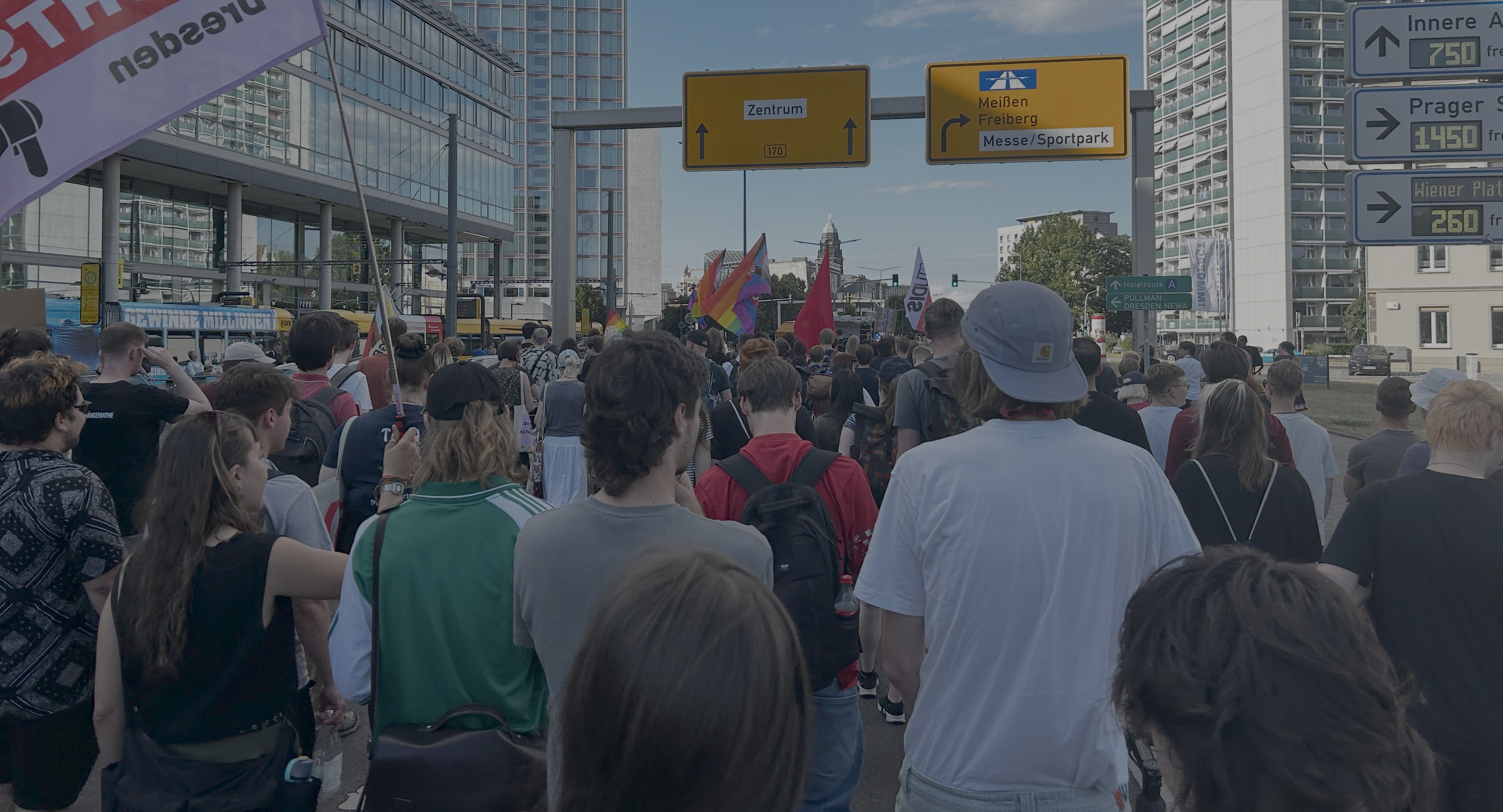 Demonstration vom 25.06.2025 gegen geplante Kürzung bei Studierendenwerken Ein Foto aus der Menge einer Demonstration aufgenommen. Menschen von sind von hinten gezeigt. Sie laufen die St. Petersburger Straße in Dresden entlang. Es sind verschiedene Fahnen, inklusive Pride-Flaggen zu sehen.